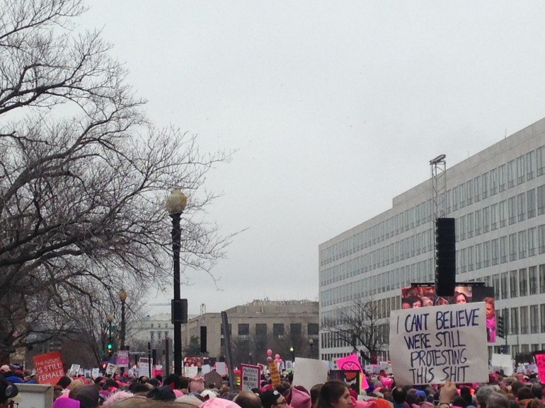 A large group of people at the womens march on washington. a sign reads 'I can't believe we're still protesting'.