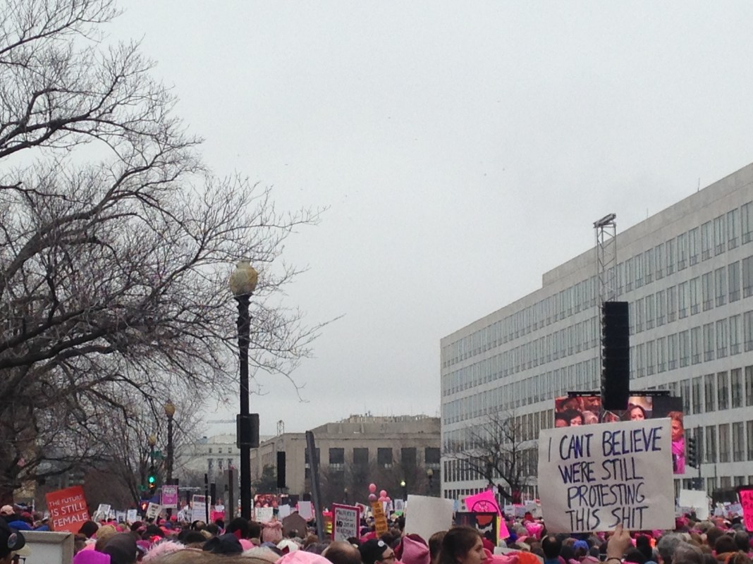 A large group of people at the womens march on washington. a sign reads 'I can't believe we're still protesting'.