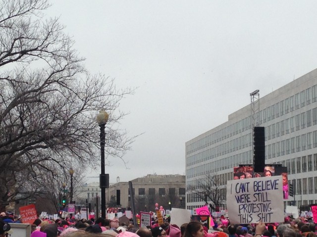 A large group of people at the womens march on washington. a sign reads 'I can't believe we're still protesting'.