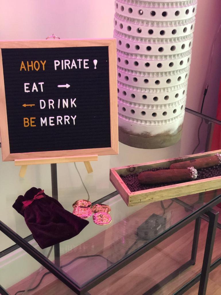 Sign-that-says-ahoy-pirate-eat-drink-and-be-merry-in-front of-gold-coins-and chocolate-cigars